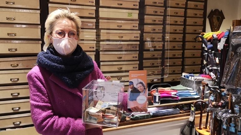 Geschäftsbesitzerin mit Spendenbox für das Flüchtlingsprojekt Ute Bock